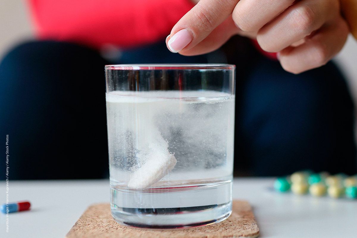 Frau hinter einem Glas mit Wasser, in dem sich eine braustablette sprudelnd auflöst. Kinder finden die Prozedur spannend, weswegen Braustabletten kindersicher verwahrt werden sollten.