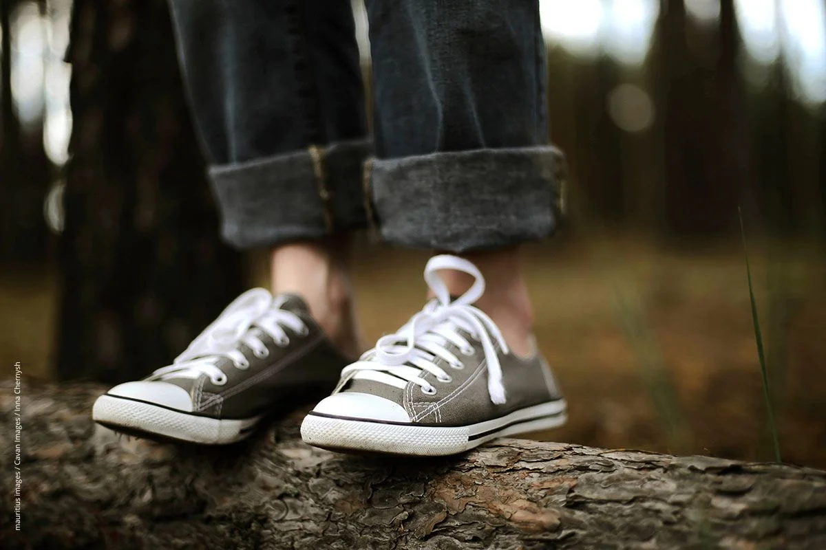 Junge steht auf einem liegenden Baumstamm im Wald. Seine Fußknöchel sind unbedeckt - ein ideales Ziel für Zecken.