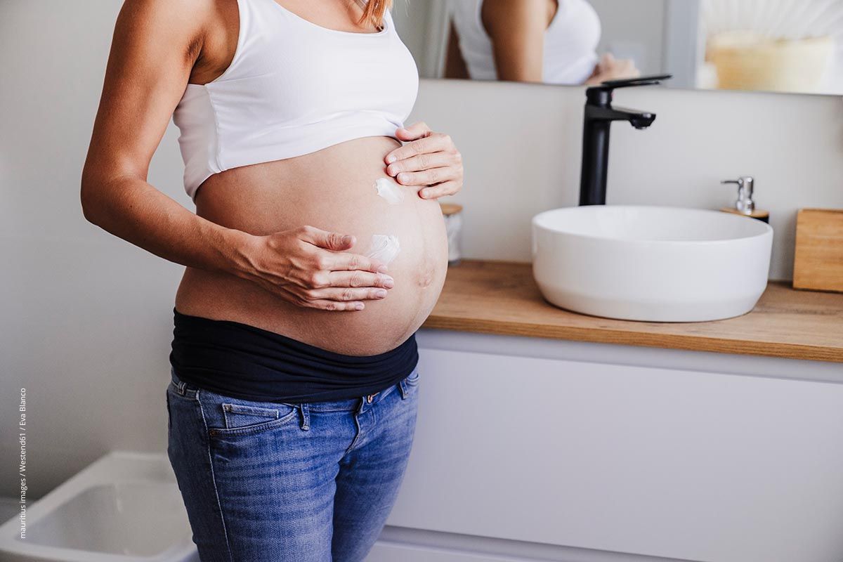 Schwangere cremt ihren Bauch ein. Eine Schwangerschaft ist eine Herausforderung für die Bauchhaut. Gute Hautpflege hilft.