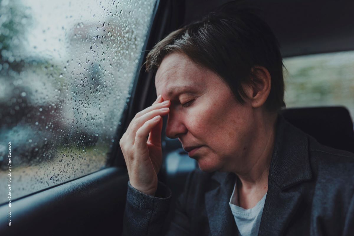 Eine erschöpfte Frau sitzt auf der Rückbank eines Autos, sie hat ihre Stirn in die Hand gelegt.
