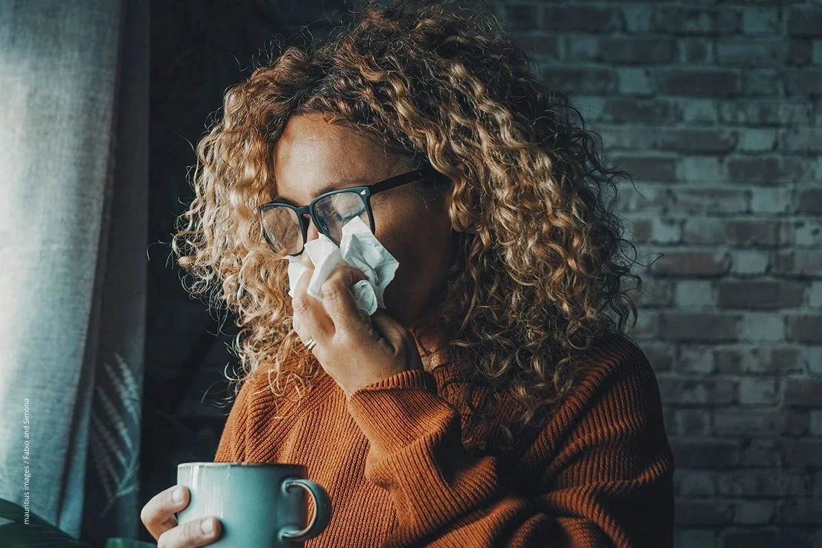 Frau niest in ein Taschentuch. Das tut leider nicht jede*r. Eine Impfung gegen Influenza-Viren schützt vor der Ansteckung.