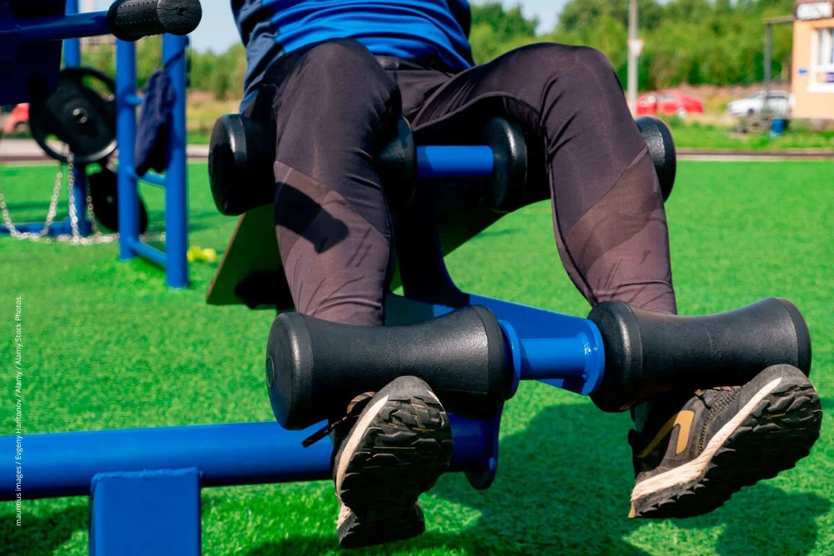 Person beim Beintraining auf einem Outdoor-Fitnessplatz. 