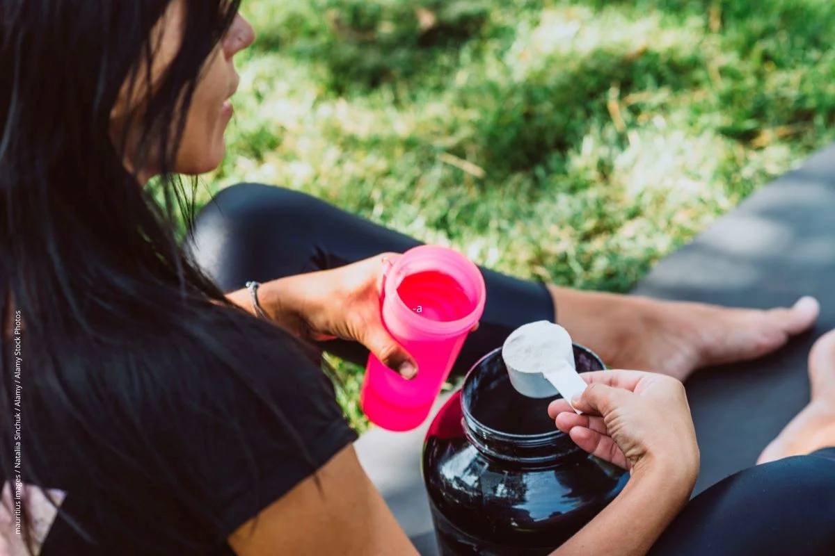 Frau sitzt auf Trainingsmatte und bereitet sich einen Protein-Shake zu. 