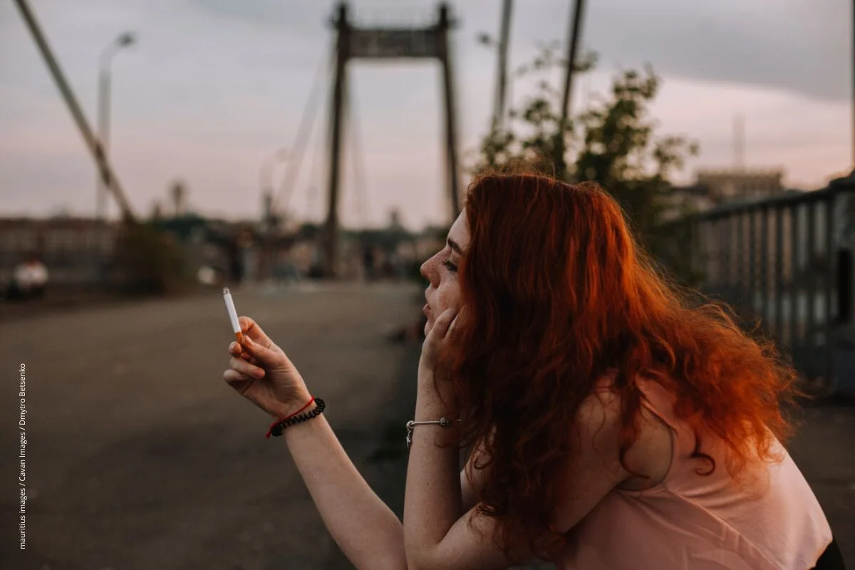 Eine rothaarige Frau schaut auf ihre Zigarette.