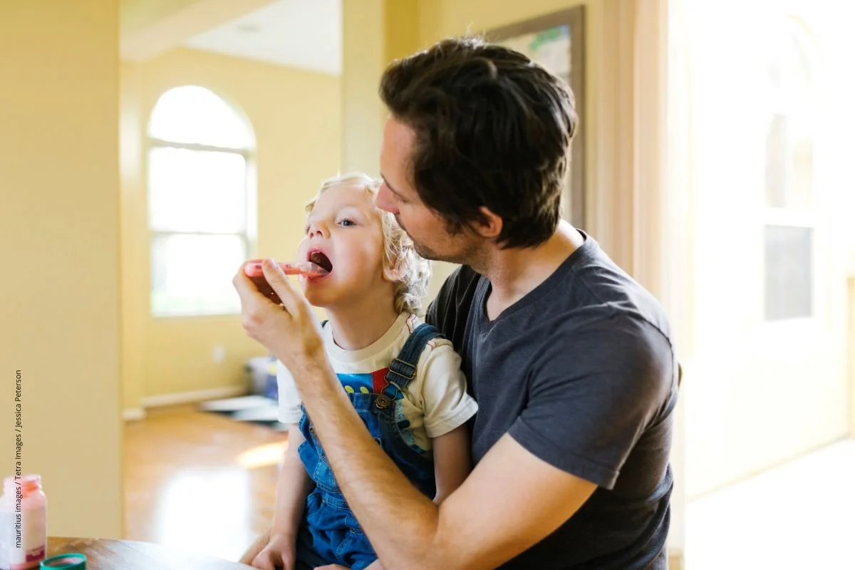 Ein Vater gibt seinen Sohn Antibiotikum-Saft mit einem Dosierlöffel ein.