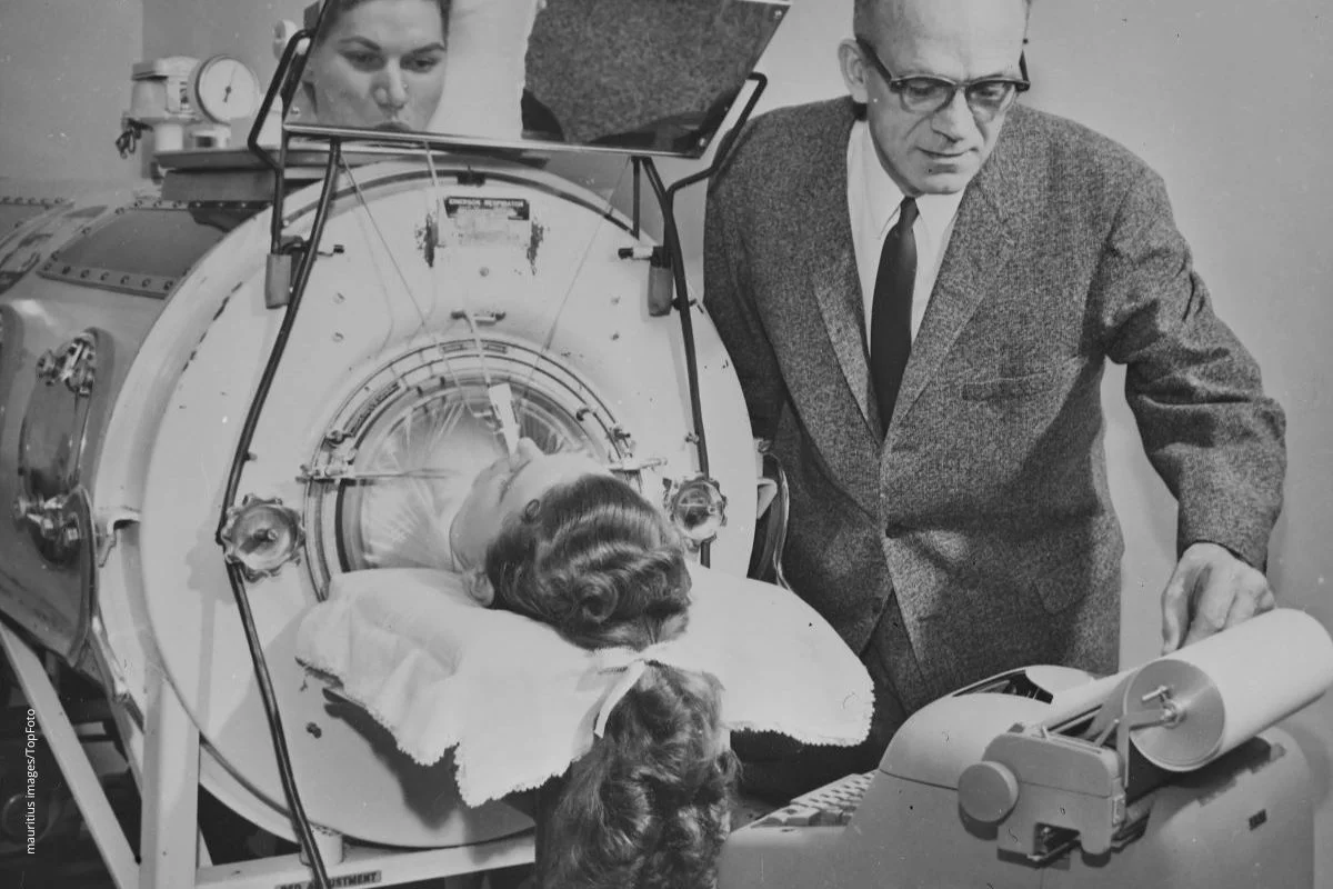 Historisches Bild eines Polio-Patienten in einer Eisernen Lunge. Soganennte Kinderkrankheiten können schwere Folgen haben, darum ist Impfen so wichtig.