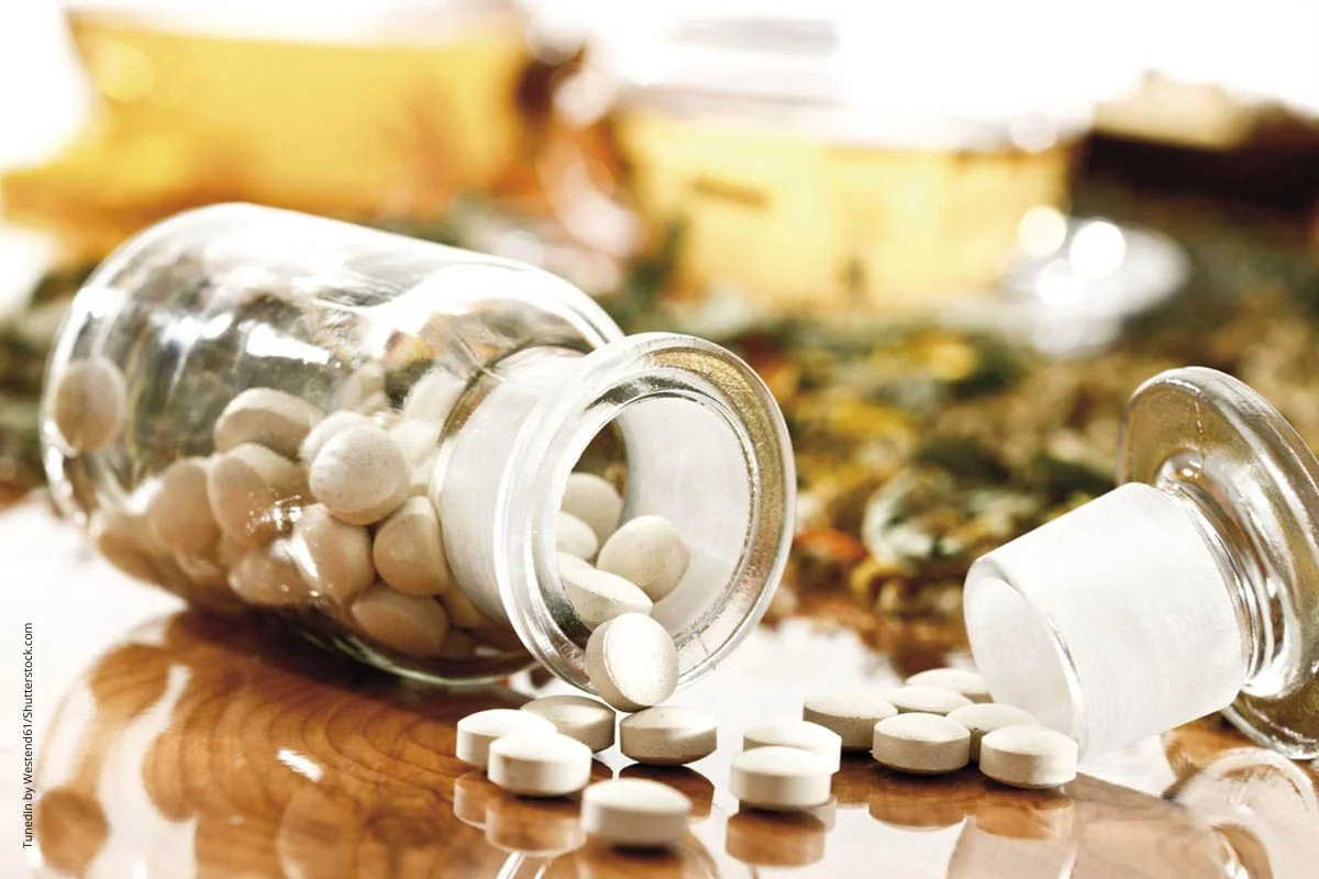 Glas mit Tabletten mit Samen und Blättern auf einem Tisch. Die Wirkstpffe von Pflanzen waren die BAsis für die ersten Medikamente und sind es noch immer.