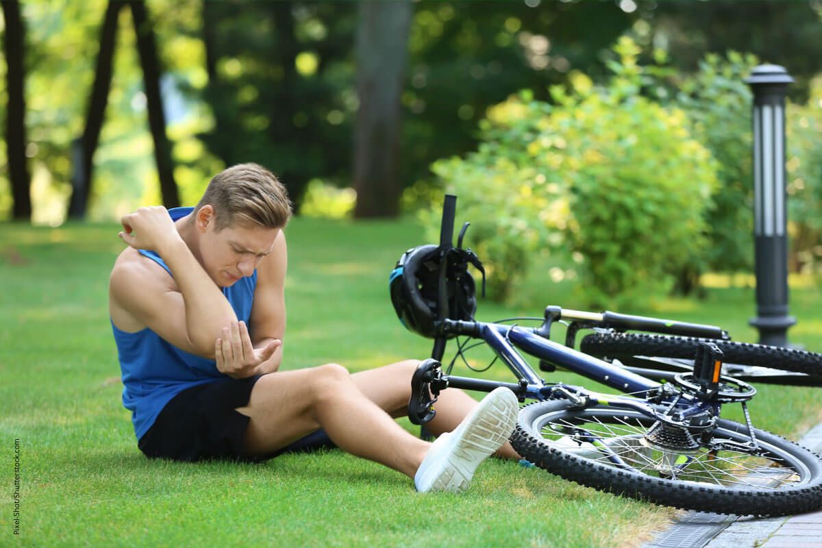 Mann inspiziert seinen Ellenbogen nach einem Radsturz. Stürze sind eine häufige Ursache für Ellenbogenbeschwerden.