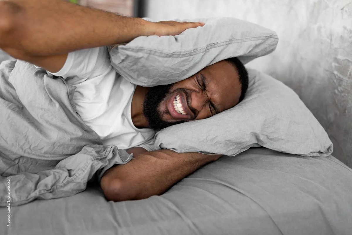 Mann presst sich im Bett das Kopfkissen gegen die Ohren. Bei Tinnitus hilft das wenig, die Geräusche entstehen im Ohr.