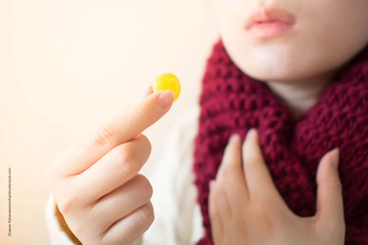 Frau mit Schal hÃ¤lt eine Lutschtablette. Tabletten gegen Halschmmerzen enthalten oft entzÃ¼ndungshemmende Wirkstoffe.