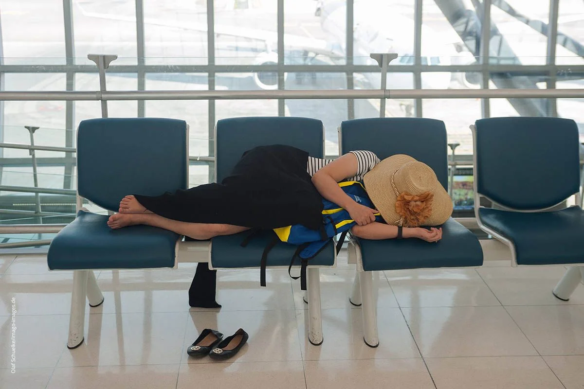 Schlafende Urlauberin auf einer Wartebank im Flughafen. Der Jetlag kann Fernreisende sehr beintrÃ¤chtigen.